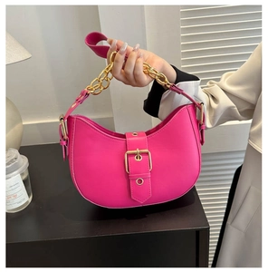 Detail of rose red crescent shoulder bag featuring bold gold chain handle and buckle
