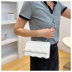 Detail of white wave-flap crossbody bag with adjustable silver chain and metal ball buckle
