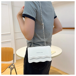 Side view of a white chain shoulder bag with wavy texture on a model in a cozy room