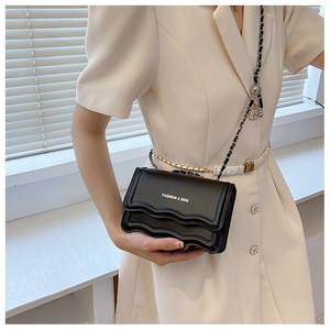 Detail of black crossbody bag featuring wavy edges and leather-interwoven chain strap