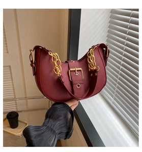 Detail of dark red half-moon bag with gold chain strap and large buckle ornament