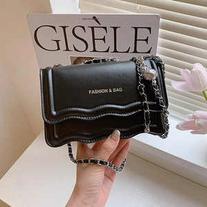 Chic black flap bag with silver chain strap and hollow metal ball on a fashion magazine