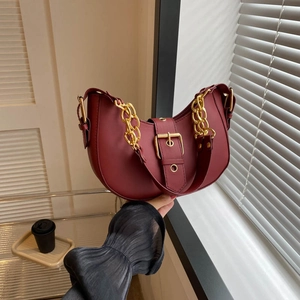Deep burgundy half-moon shoulder bag with bold gold chain and buckle on minimalist background