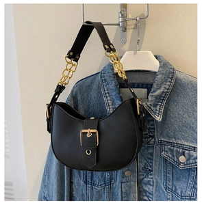 Détail du sac demi-lune en cuir noir avec chaîne dorée et boucle sur une veste en jean