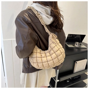 Detail of beige quilted puffer bag with ruffled strap shown on shoulder with stylish jacket