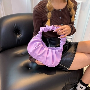 Lilac pleated leather hobo bag with a soft crescent shape on a luxury black sofa