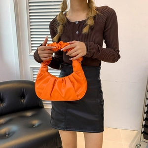 Vibrant orange ruched dumpling handbag in half-moon shape held by a model