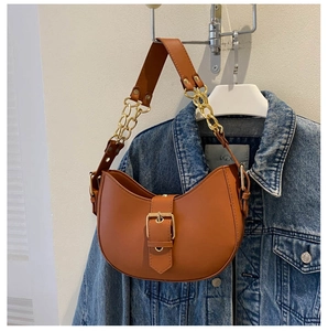 Détail d'un sac besace marron caramel avec boucle dorée sur fond de veste en jean