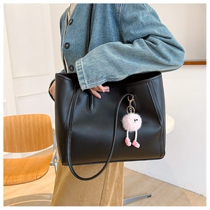 Close-up of black leather tote bag with a pink plush charm on a wooden chair