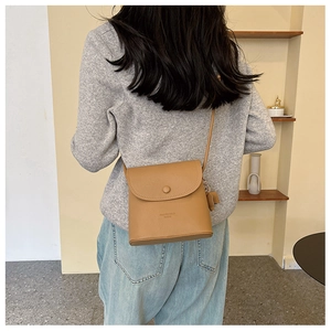 Detailansicht einer braunen Umhängetasche aus Leder mit Litschi-Muster und Bärenanhänger