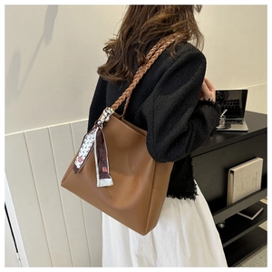 Brown leather tote bag with woven shoulder strap and silk scarf detail shown on a model