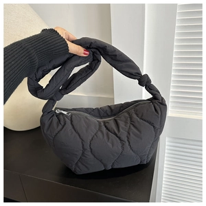 Detail of black quilted nylon dumpling bag featuring a padded puffy texture and knotted strap