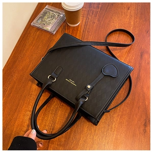 Détail du sac à main matelassé noir avec lettrage doré posé sur une table en bois
