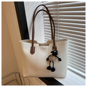 Detail view of cream tote bag with brown straps and a cute sheep plush charm accessory