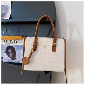 Détail d'un cabas matelassé beige avec bordure marron et breloque cœur sur un support