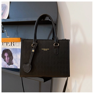 Détail d'un sac cabas noir matelassé avec lettrage doré et breloque cœur en cuir