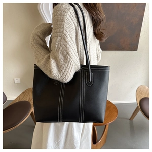Detail of black tote bag with white contrast stitching on model's shoulder in cafe setting