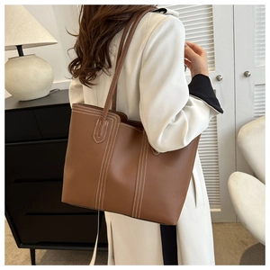 Detail of brown leather tote bag featuring striking white contrast vertical stitching