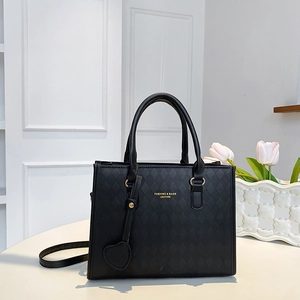Élégant sac cabas noir matelassé avec lettrage doré et breloque coeur sur un bureau blanc