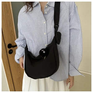 Detail of black crescent crossbody bag with wide strap and plush spirit charm accessory