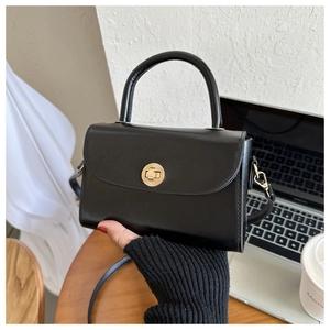 Macro detail of black leather crossbody bag featuring gold sunburst twist-lock closure