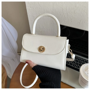 Close-up of a creamy white structured handbag with a gold twist lock and rigid handle