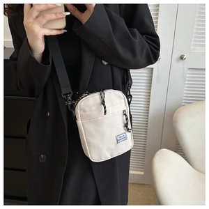 Detailed shot of beige nylon crossbody bag featuring HELLO WEEKEND text and black straps