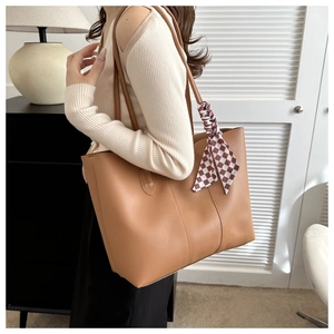 Brown leather tote bag detail with vertical stitching and red checkered silk scarf handle