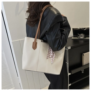 Detail of a beige leather tote bag with dark brown handles and a checkered silk scarf
