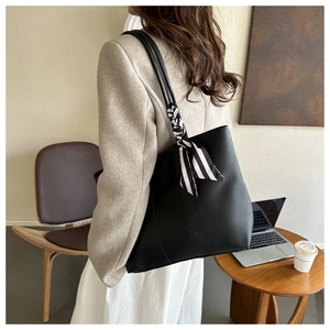 Detailed view of black leather tote bag with striped ribbon worn by model in a cafe