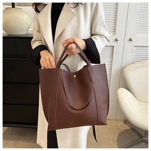 Detail of dark brown tote bag featuring long straps and a gold circular magnetic buckle