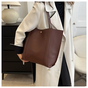 Detail of a large brown faux leather tote bag with vertical stitching and gold metal buckle