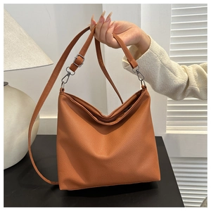 Brown faux leather bucket tote bag with litchi texture held by a model in a room
