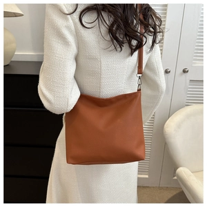 Brown litchi grain bucket bag with slim shoulder strap worn by a model in a minimal style