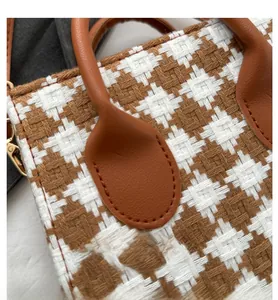 Detail of houndstooth woven fabric and brown leather handle with golden metal buckle