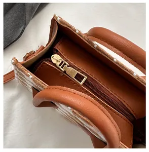 Close-up of smooth gold metal zipper closure on brown plaid texture handbag