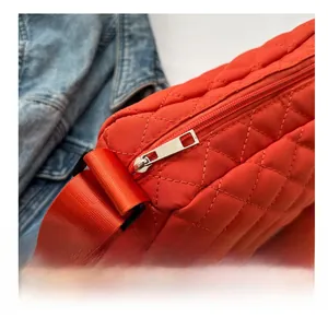 Close-up of smooth silver zipper on red quilted nylon shoulder bag with denim backdrop