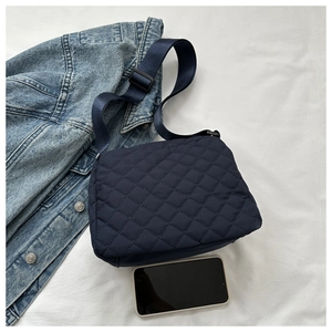 Detail view of navy quilted crossbody bag with adjustable strap next to a smartphone