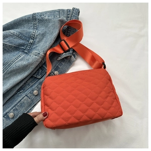 Detail of orange quilted crossbody bag with adjustable strap and diamond lattice pattern