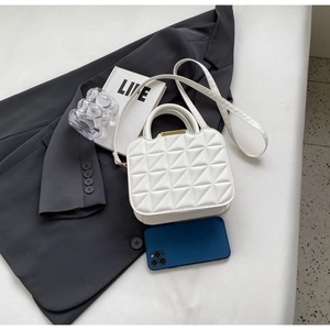 Flat lay of white quilted crossbody bag with gold metal clasp on a minimalist desk