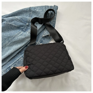 Detail of black quilted crossbody bag with wide nylon strap on denim jacket background