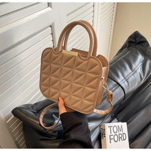 Detail of beige quilted bag with wave-edge flap and golden metal bar handle