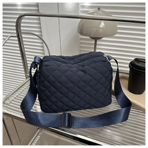 Close-up of a blue quilted crossbody bag featuring diamond stitching and a metal zipper