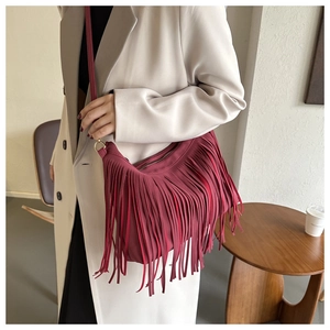 Burgundy faux suede fringe bucket bag worn crossbody in a minimalist interior setting