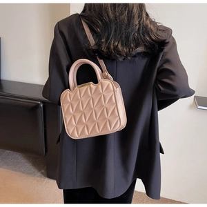Detail of beige quilted shoulder bag with rigid handle and gold trim worn by model