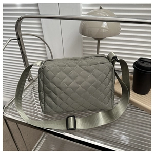 Detail of sage green quilted nylon bag with adjustable wide strap on modern shelf