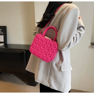 Close-up of a magenta quilted crossbody bag on a model wearing a grey suit jacket