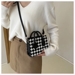 Detail of black and white tweed plaid handbag with golden hardware and leather straps