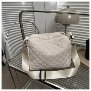 Detail of a creamy quilted crossbody camera bag with wide strap on a modern glass shelf