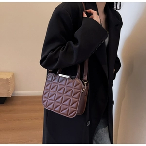 Detail of a dark brown quilted handbag with 3D geometric patterns on a shoulder model